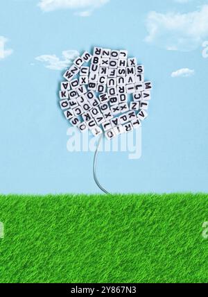 Fleur faite de cubes de lettres fleurit dans l'herbe sous un ciel bleu avec des nuages Banque D'Images