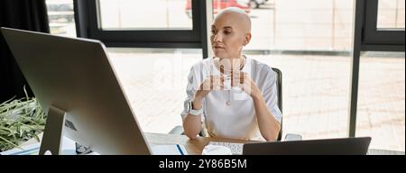 Une jeune femme chauve dans des vêtements élégants est assise à son bureau, profondément dans la contemplation, engagée dans le travail. Banque D'Images