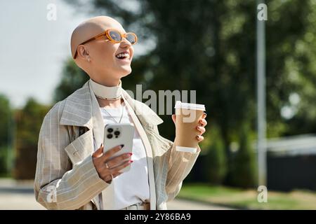 La jeune femme sourit largement tout en tenant un smartphone et une tasse à café, exsudant la joie. Banque D'Images