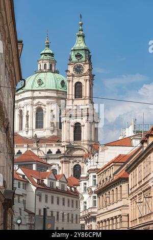 La tour ornée de St. L'église Nicolas s'élève au-dessus d'une charmante rue de Prague, son horloge fait face à un témoignage du temps Banque D'Images