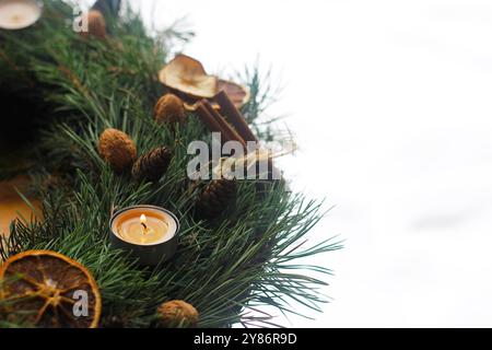 Gros plan d'une couronne de l'Avent faite maison avec une bougie de thé brûlante décorée avec de l'orange séchée, de la cannelle entière et des noix sur fond blanc Banque D'Images