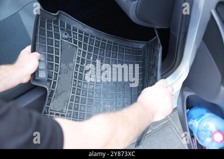 Homme prenant tapis de voiture en caoutchouc noir de l'auto, gros plan Banque D'Images