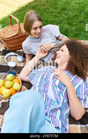 Deux amis partagent des moments joyeux lors d’un pique-nique ensoleillé rempli de fruits frais et de rires. Banque D'Images