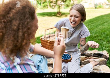 Deux amis partagent des moments joyeux, des collations et des rires par une journée ensoleillée dans un jardin luxuriant. Banque D'Images