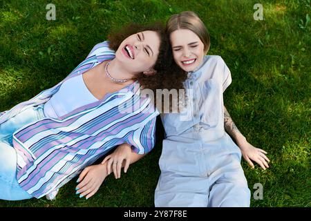 Deux jeunes femmes apprécient la compagnie, riant ensemble sur l'herbe verte. Banque D'Images
