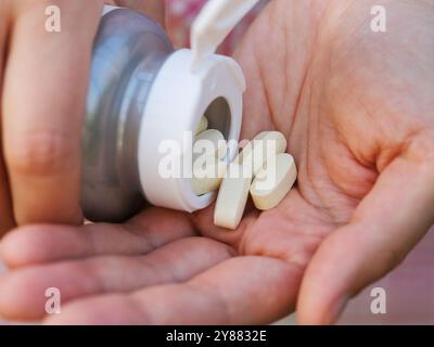 Une femme verse des comprimés de taurate de magnésium d'une bouteille dans la paume de sa main. Gros plan. Banque D'Images