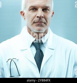 Professionnel de la santé mature avec une expression sérieuse pose dans une blouse de laboratoire blanche avec un stéthoscope autour de son cou Banque D'Images