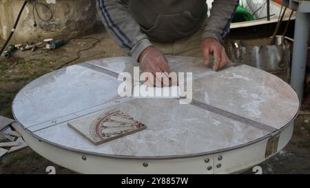 homme posant des carreaux décoratifs découpés sur une table ronde de table maison, carrelage de meubles avec des carreaux à motifs géométriques Banque D'Images