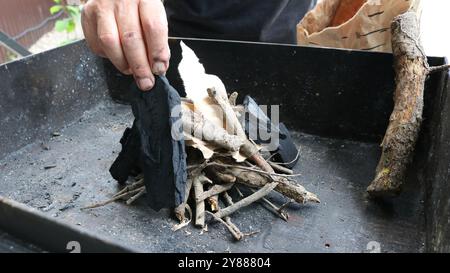 Les mains placent un morceau de papier brun clair parmi de petits bâtons et des brindilles de couleur variant du beige au brun foncé, qui sont placés sur un métal noir Banque D'Images