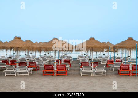 Parasols palmiers et chaises longues sur la plage de la mer Méditerranée en Espagne. Banque D'Images