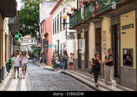 Les gens marchent à travers une rue commerçante étroite confortable dans le centre historique de Funchal. Banque D'Images