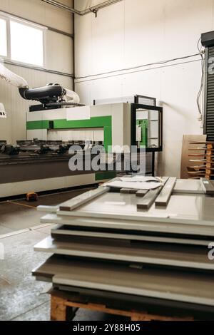 Les panneaux de bois fraîchement coupés s'empilent à côté d'un routeur CNC dans une usine lumineuse. La machine est utilisée pour la coupe précise dans la production de meubles Banque D'Images