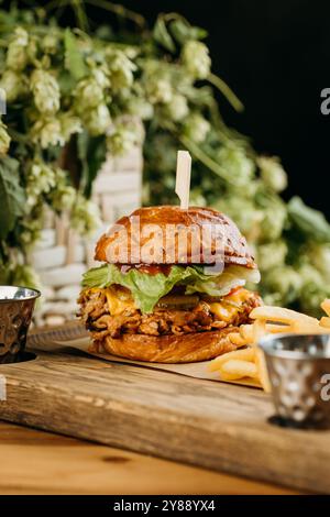 Délicieux burger de porc effiloché avec laitue fraîche et fromage fondu servi avec des frites à bord Banque D'Images
