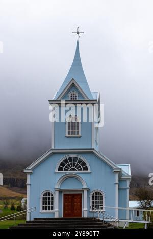 L'église bleue de Seydisfjordur (Seydisfjardarkirkja), vue extérieure de la façade du bâtiment bleu vif, montagnes brumeuses en arrière-plan, Islande. Banque D'Images