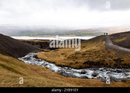 Vallée de la rivière Hengifossa avec des silhouettes de personnes sur un sentier de randonnée à Fljotsdalshreppur, dans l'est de l'Islande. Lac glaciaire Lagarfljot et pont. Banque D'Images