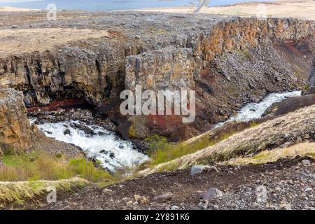 Vallée de la rivière Hengifossa à Fljotsdalshreppur, dans l'est de l'Islande avec des formations rocheuses rouges et brunes, des falaises et le lac glaciaire Lagarfljot en arrière-plan. Banque D'Images