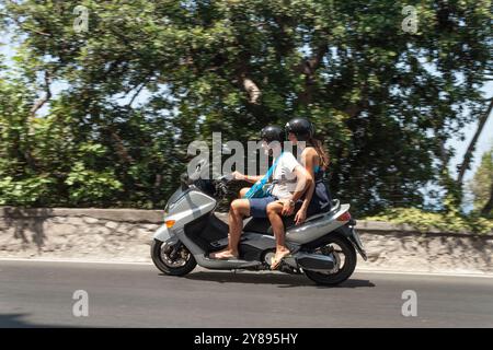 couple monte un scooter sur une journée ensoleillée devant un mur beige avec des arbres sorrento italie Banque D'Images