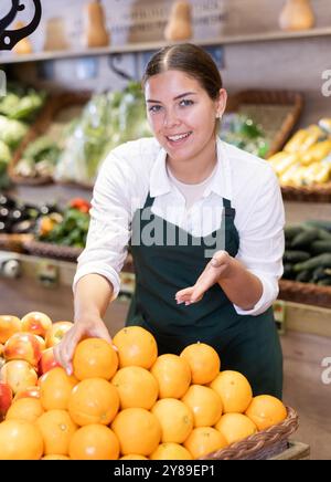 Jeune vendeuse offrant des oranges dans le magasin de fruits et légumes Banque D'Images