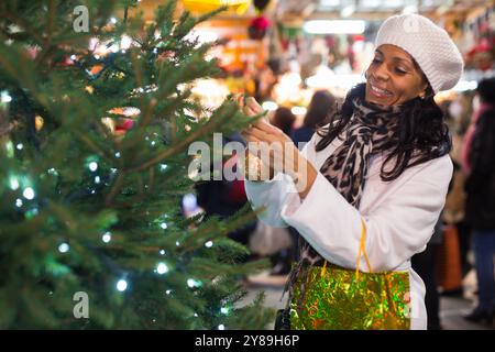 Femme hispanique gaie à la recherche d'un arbre de Noël sur un marché en plein air Banque D'Images