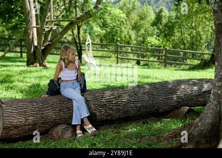 Une fille est assise sur une bûche avec les jambes croisées dans une ferme Banque D'Images