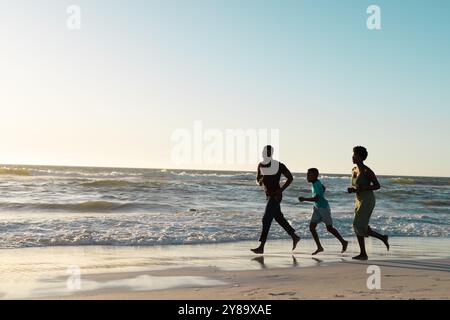 Joyeux père afro-américain et mère avec son fils courant sur la plage contre le ciel au coucher du soleil Banque D'Images