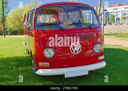 La fourgonnette volkswagen Kombi rouge est garée sur un terrain herbeux avec des bâtiments en arrière-plan Banque D'Images