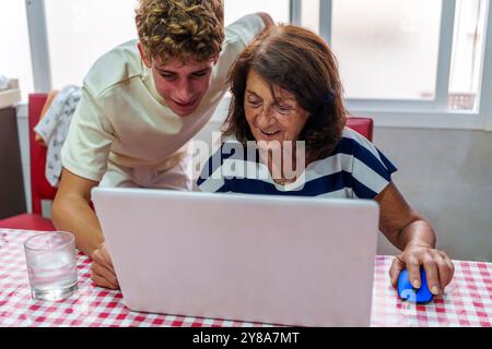 Adolescent apprenant à sa grand-mère de 70 ans à utiliser un ordinateur portable, Bridging the Digital Divide Banque D'Images