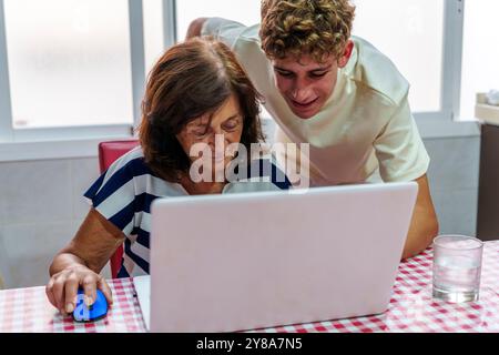 Adolescent apprenant à sa grand-mère de 70 ans à utiliser un ordinateur portable, Bridging the Digital Divide Banque D'Images