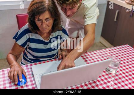 Adolescent apprenant à sa grand-mère de 70 ans à utiliser un ordinateur portable, Bridging the Digital Divide Banque D'Images