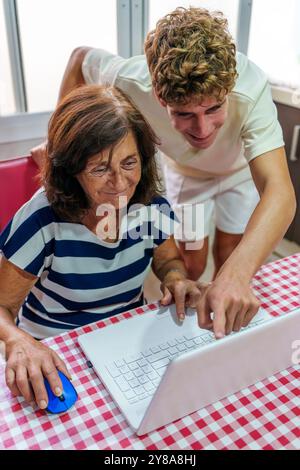 Adolescent apprenant à sa grand-mère de 70 ans à utiliser un ordinateur portable, Bridging the Digital Divide Banque D'Images