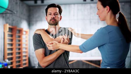 Physiothérapeute féminine donnant Un exercice d'épaule d'homme à la clinique Banque D'Images