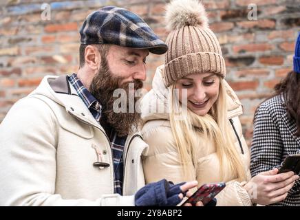 Couple profitant d'une journée d'hiver ensemble tout en souriant à leurs smartphones. L'image capture un moment de connexion confortable et joyeux pendant le se froid Banque D'Images