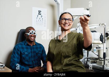 Optométriste effectuant un examen oculaire avec le patient portant des cadres d'essai dans un bureau d'optométrie moderne Banque D'Images