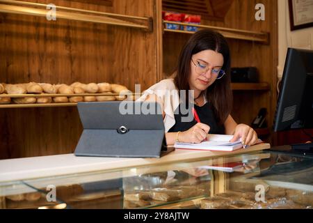 Une femme prenant des notes au comptoir d'une boulangerie pendant les heures de bureau de jour Banque D'Images