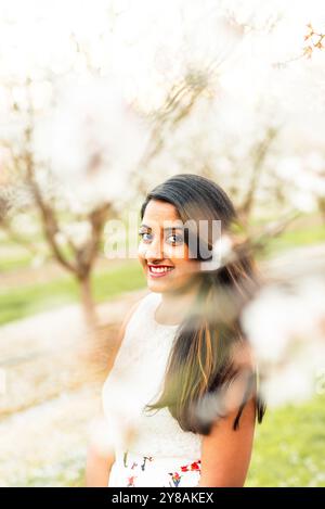 Femme souriante en robe blanche entourée de fleurs douces et floues. Banque D'Images