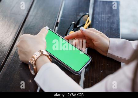 Une femme s'engageant avec un smartphone sur une table en bois avec des lunettes de soleil à proximité. Banque D'Images