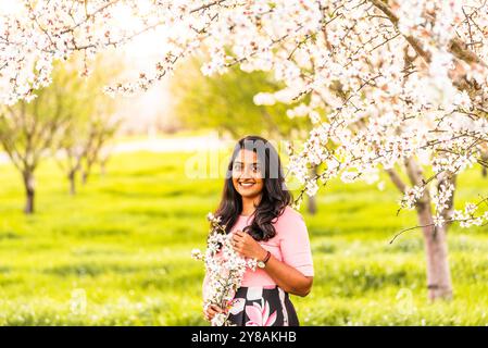 Femme souriante tenant des fleurs d'amande dans un verger en fleurs. Banque D'Images