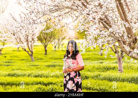 Femme souriant tout en tenant des fleurs d'amande dans un verger en fleurs Banque D'Images