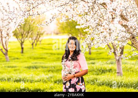 Femme souriante tenant des fleurs d'amande dans un verger en fleurs Banque D'Images