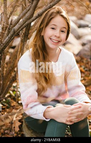 La fille blonde sourit dehors dans les feuilles d'automne de la nature et des arbres Banque D'Images