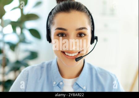Photo en gros plan d'une belle femme caucasienne brune réussie positive avec casque, travaillant comme opérateur de centre d'appels, service d'assistance client, assistant de ligne directe, coach d'affaires, sourires à la caméra Banque D'Images