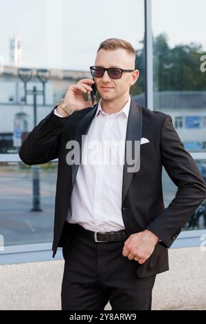 Homme élégant dans un costume élégant parlant décontracté sur son téléphone à l'extérieur. Banque D'Images