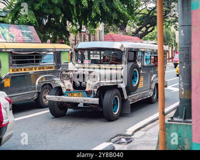 Manille, Philippines - 26 août 2019 : un jeepney dynamique conduit le long d'une rue animée, entouré de divers véhicules et d'arbres verts. Banque D'Images