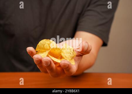 Homme mangeant des chips. Vue d'une main tenant une pile de chips striées. Tient les croustilles à la main. Restauration rapide. Malbouffe. Mode de vie malsain Banque D'Images