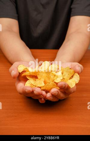 Vue d'une main tenant une pile de chips striées. Homme mangeant des chips. Tient les croustilles à la main. Restauration rapide. Malbouffe. Mode de vie malsain Banque D'Images