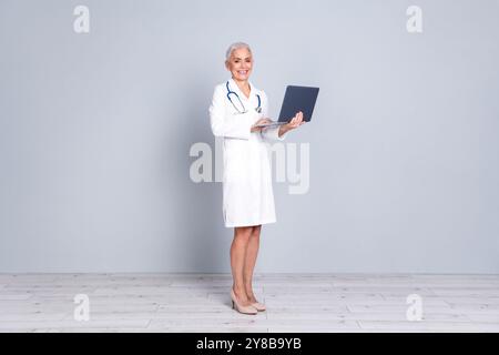 Photo de charmant médecin professionnel spécialiste qualifié porter manteau blanc tenir netbook isolé sur fond de couleur grise Banque D'Images