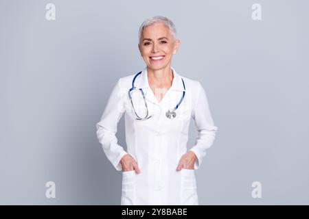 Photo de charmante femme médecin qualifiée porter des mains de robe blanche dans des poches isolées sur fond de couleur grise Banque D'Images