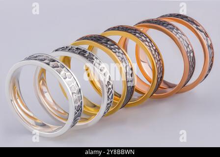 Anneaux de mariage faits de trois métaux. Un ensemble de six anneaux sur fond blanc. Bagues en or et argent avec une surface rugueuse. Banque D'Images