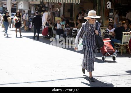 Jérusalem, Israël - 1er octobre 2024, Une femme âgée élégamment habillée en costume classique et chapeau marche à travers la foule au marché Mahane Yehuda. Banque D'Images