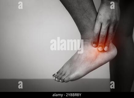 Femme avec douleur aiguë à la cheville avec douleur à la jambe sur fond gris, traitement de la cheville et de la jambe, massage féminin de son spasme musculaire de la cheville, soins de santé et médical Banque D'Images